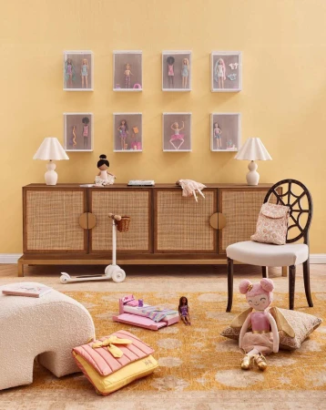 Doll collection display: Dolls in cases mounted on a wall above a wooden console with doll accessories and toys in a kids' playroom.