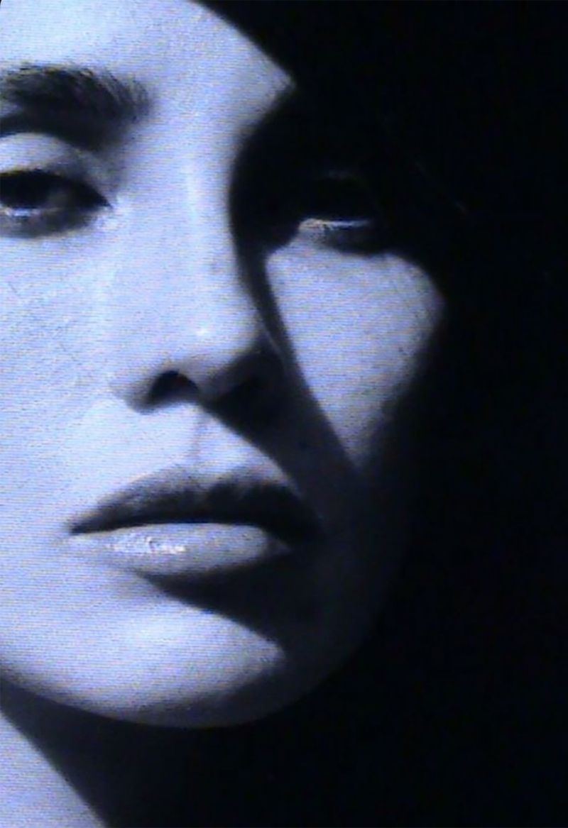 Close-up portrait of an adult female's face in a studio with contrasting light and shadows, emphasizing her features in a minimalist composition.