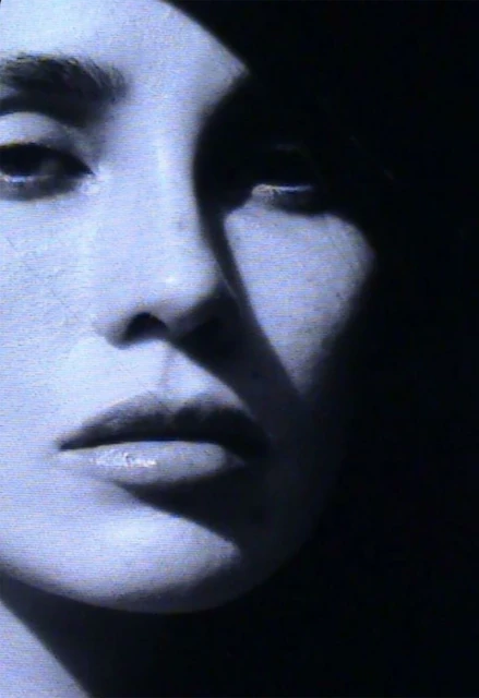 Close-up portrait of an adult female's face in a studio with contrasting light and shadows, emphasizing her features in a minimalist composition.