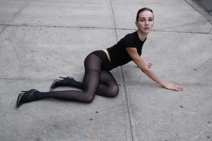 Model Mimi Flores in black top and tights posing on concrete pavement for project Facilidad Gozo y Gloria