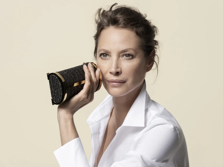 Elegant woman in white shirt holds a black and gold woven purse in a beauty shot against a light beige background. 