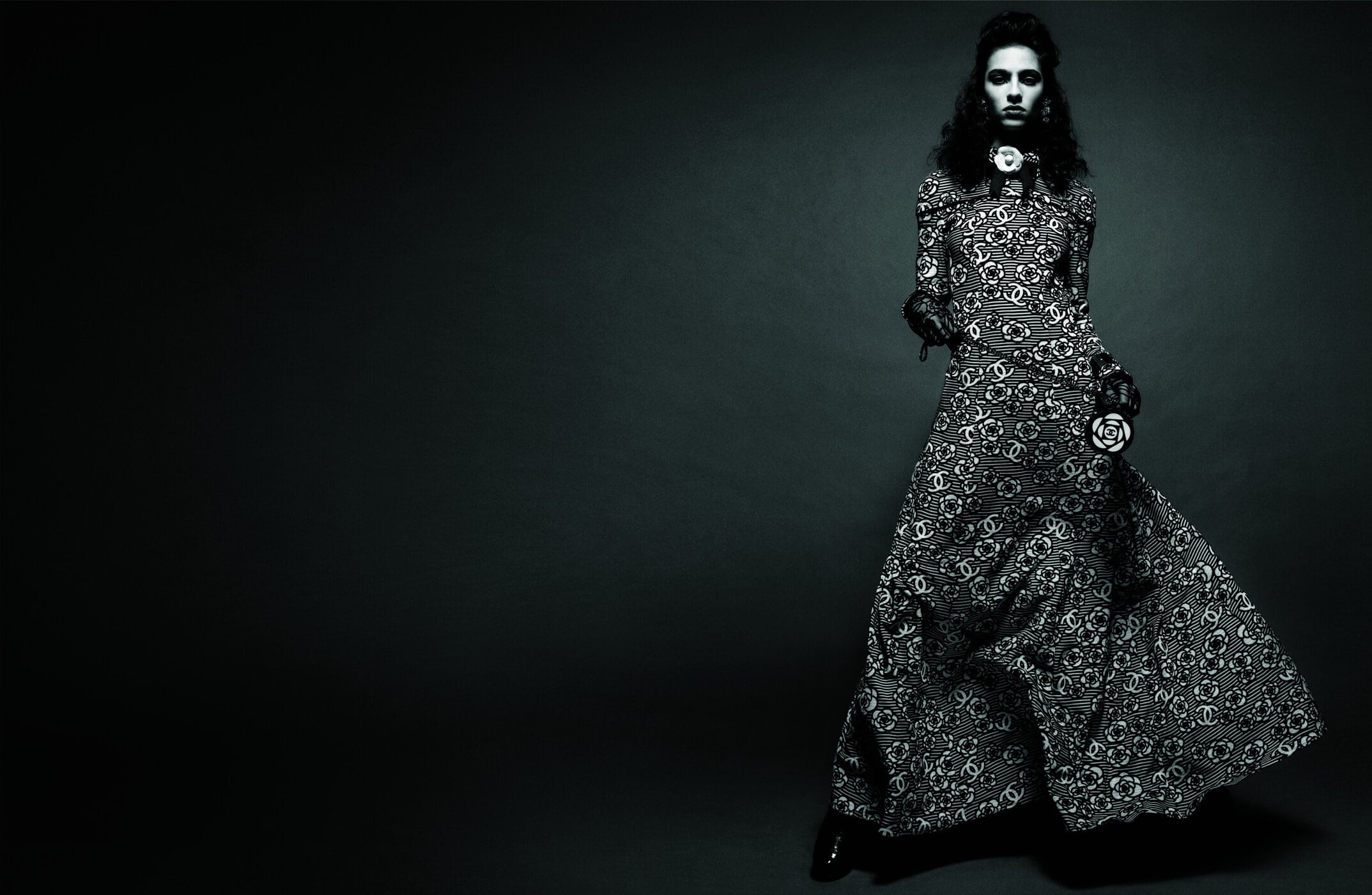 A female model poses in a patterned dress with a dark background. The studio shot highlights fashion and style.
