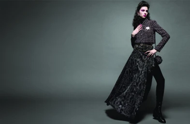 Loli-Bahia poses in a black cropped tweed jacket and patterned draped skirt against a grey backdrop for Chanel.
