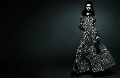 Model Loli-Bahia in a printed maxi dress against a dark studio background for Chanel Fall 2023.