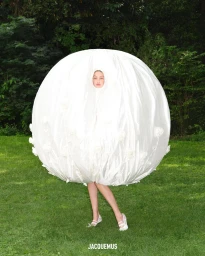 Model Gigi Hadid wearing an oversized white spherical garment on grass for the Jacquemus Fall 2023 ad campaign.