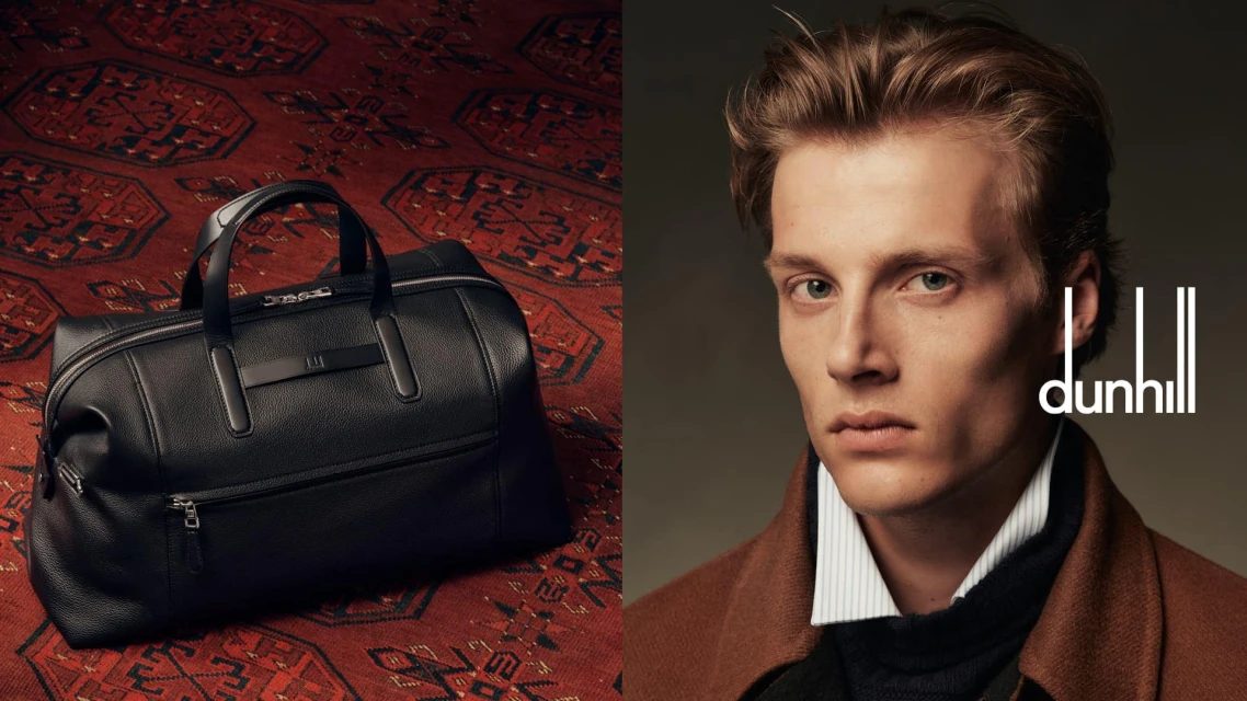 Dunhill brand ad featuring a black leather duffel bag on a red patterned rug and an adult male model wearing a brown coat.