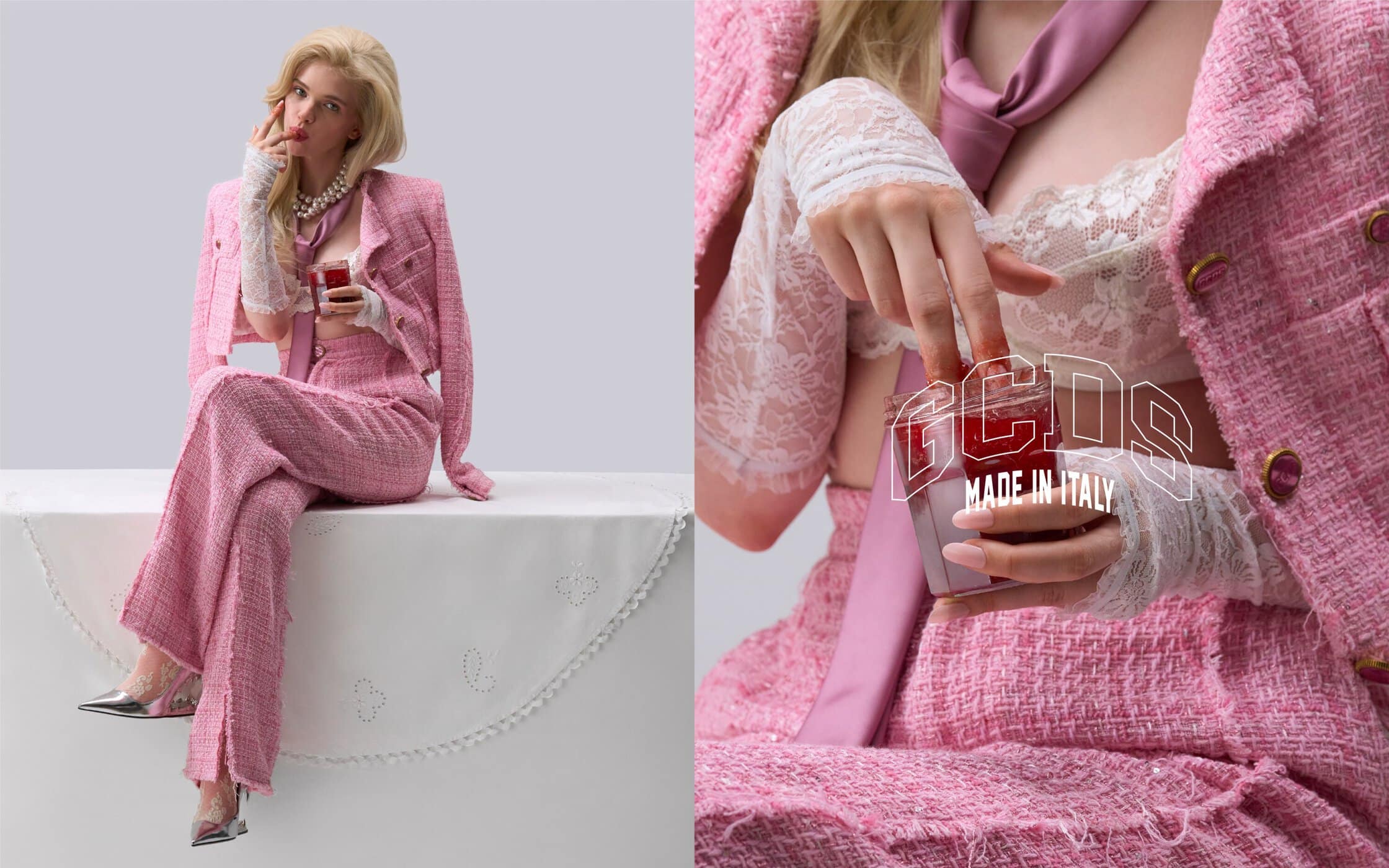 A blonde woman sits on a white table in a pink tweed suit, lace gloves, and silver heels while holding a jar of red liquid.