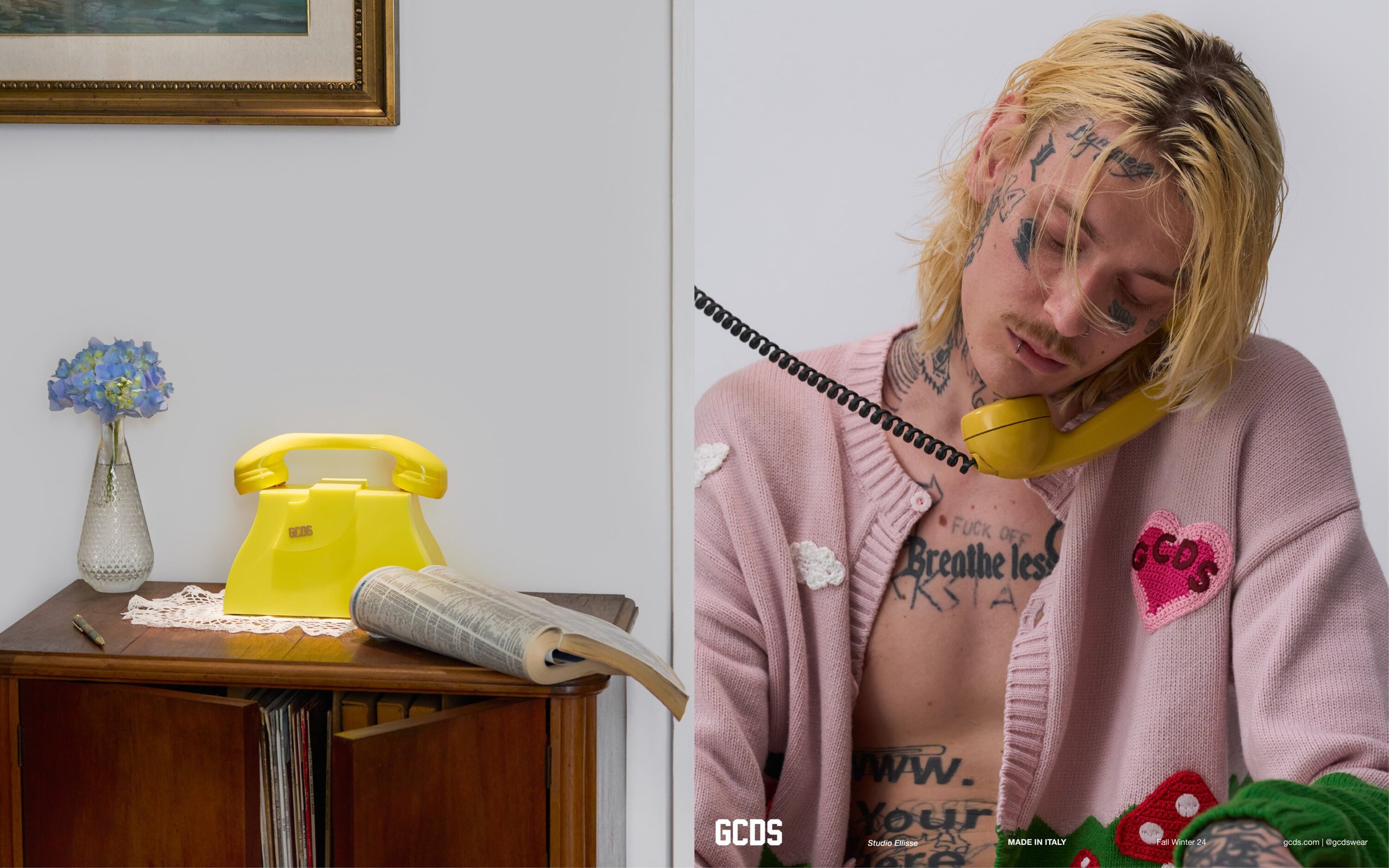 Close-up of a male model with tattoos holding a yellow telephone receiver, styled with a pink cardigan, next to a retro home setting.
