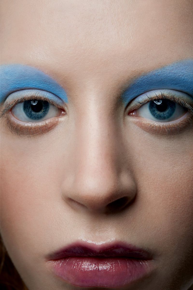 Extreme close-up of a model's face with dramatic blue eyeshadow and glossy lips, showcasing beauty and makeup in a studio setting.