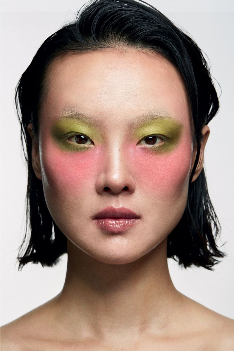 Close-up shot of a young Asian adult female model with green eyeshadow and pink blush in a beauty and fashion studio portrait.