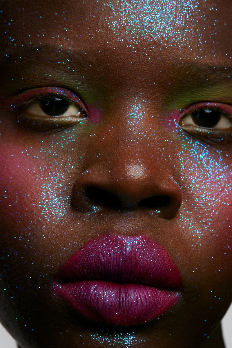 Close-up shot of an African American woman's face covered in iridescent glitter and magenta lipstick, beauty and makeup focused.