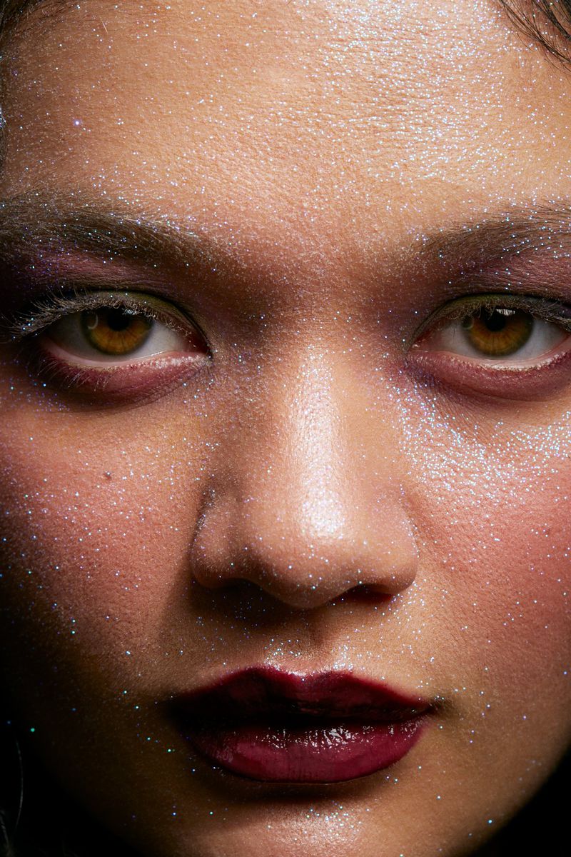Close-up portrait of an Asian woman with sparkling makeup, showcasing her brown eyes, smooth skin, and dark lipstick in a beauty shot.