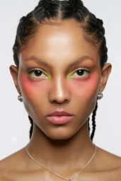 Close-up portrait of a model with braided hair, colourful eyeshadow, and silver earrings against a plain background