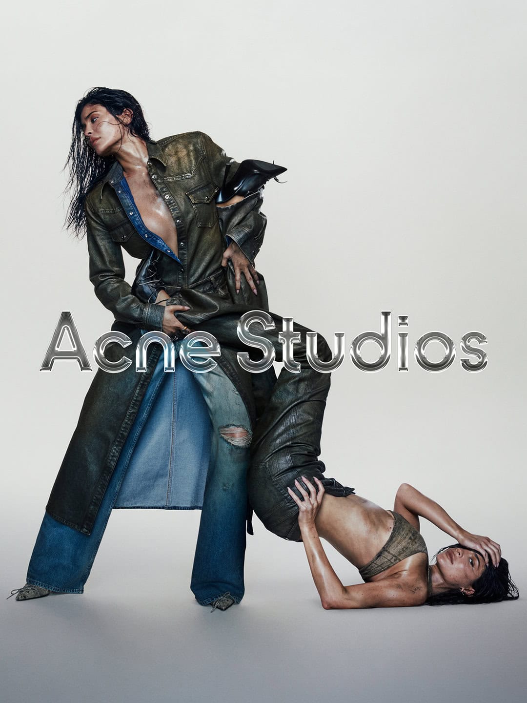Two fashion models strike poses in an indoor photo studio, wearing outfits with denim and leather textures against a neutral background.