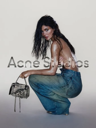 Brunette woman with wet hair poses in denim pants holding a gray snakeskin-print handbag in front of a solid beige backdrop.