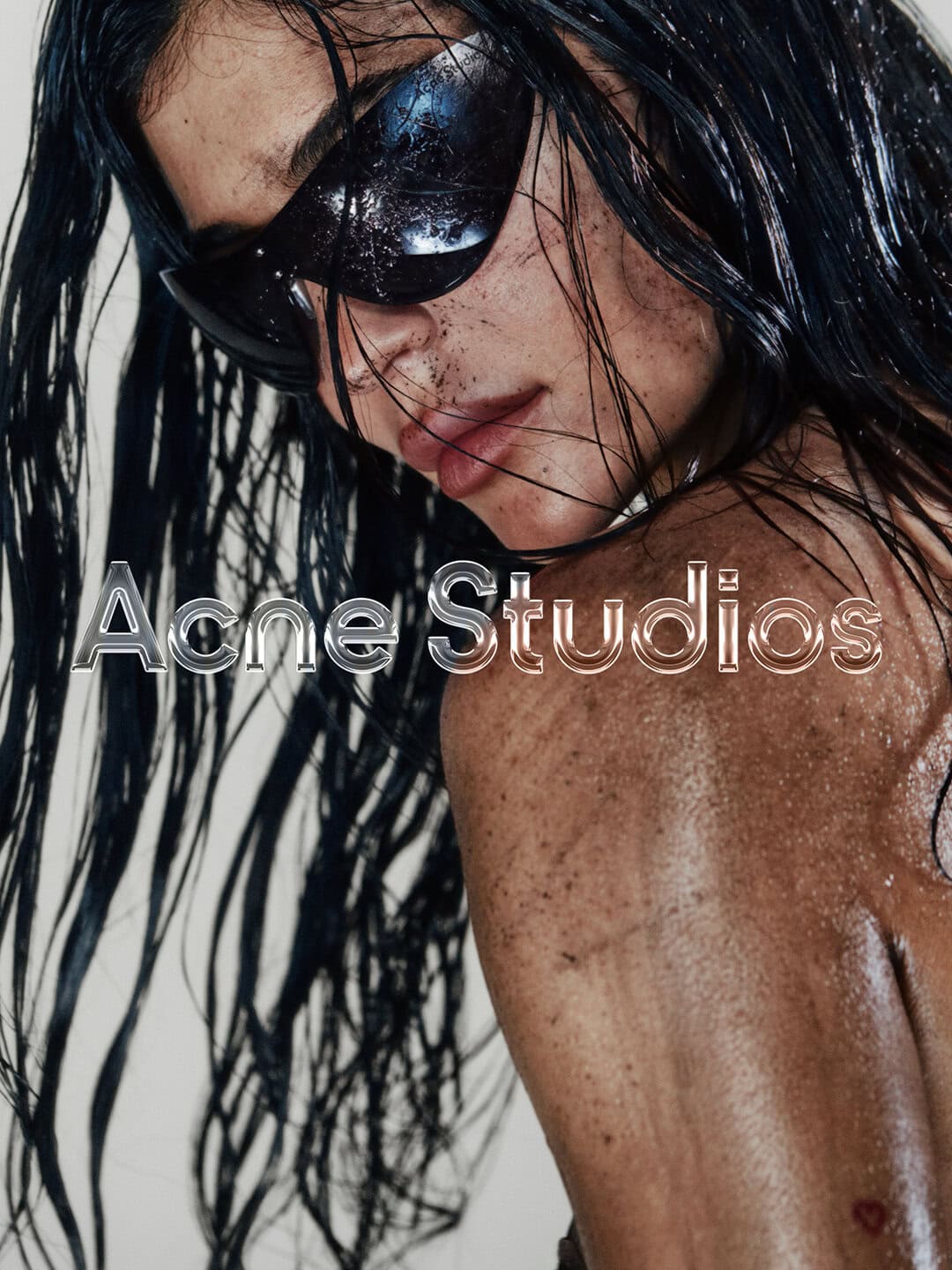 A close-up studio shot features a model with wet, black hair wearing sunglasses, facing left with the Acne Studios logo overlaid.