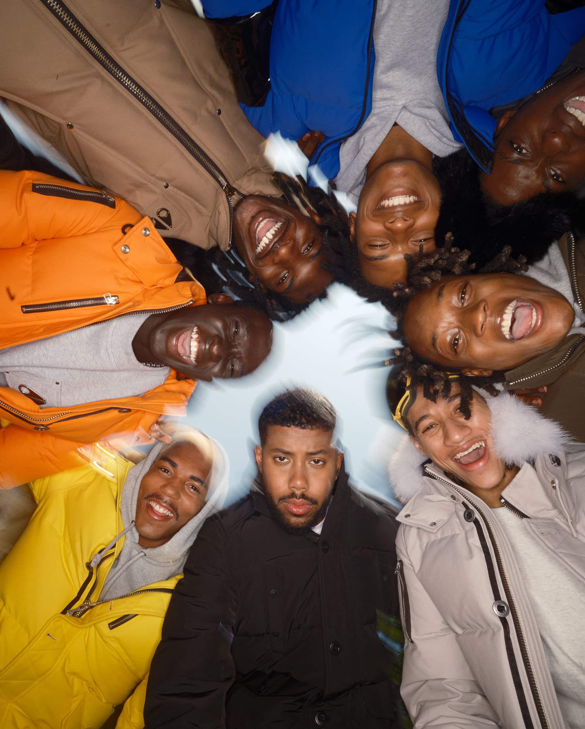 Group of smiling multi-ethnic adults in colorful winter coats lie in a circle viewed from above in casual pose, outdoors.