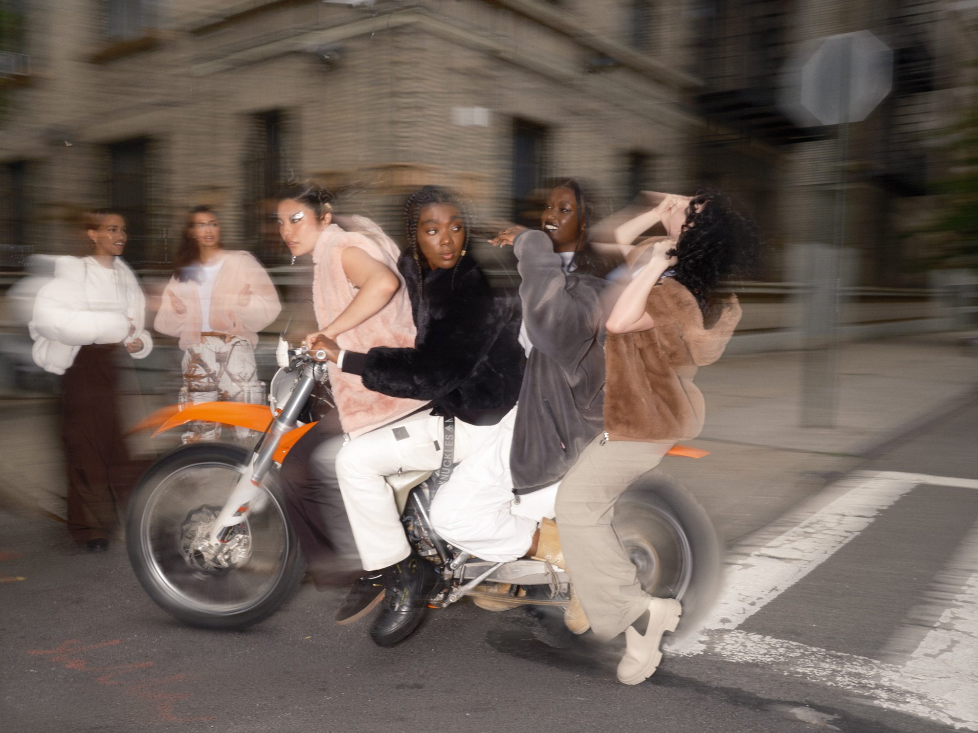 A group of young adult fashion models ride a motorcycle down an urban street with soft focus and motion blur.