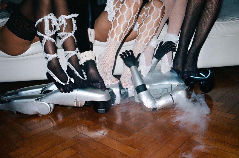 Group of women wearing fishnet stockings and lace garters sitting on a robot with smoke, showcasing a blend of fashion and technology.