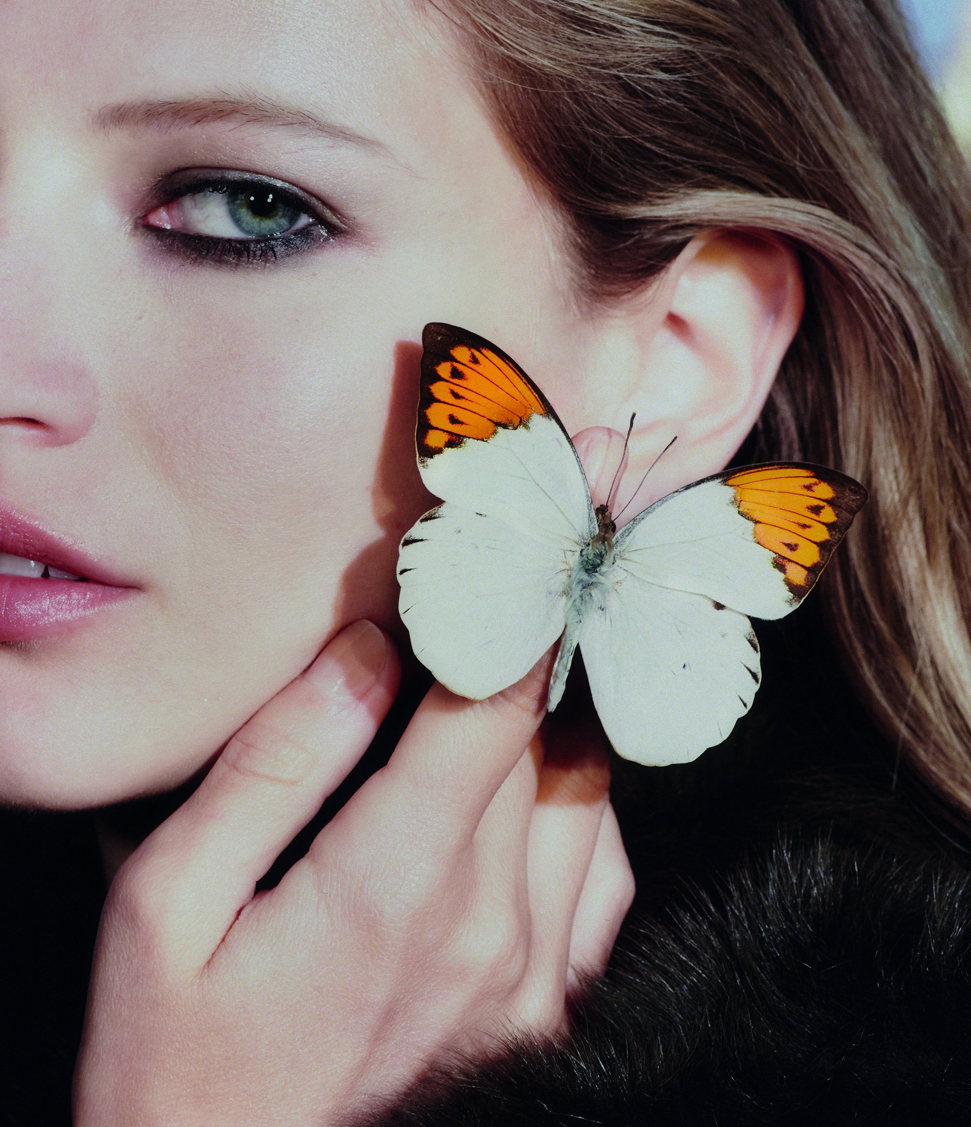 Close-up of a fair-skinned woman with a butterfly on her cheek, showing beauty and nature elements in a portrait format.