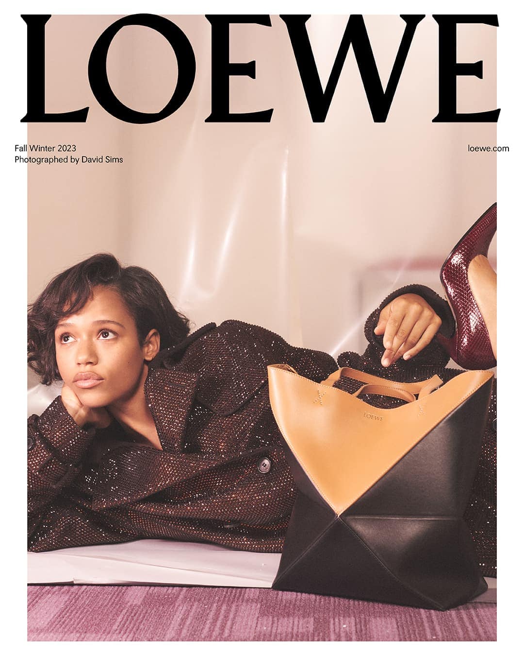 Model lying down with a black and tan leather tote bag for the Loewe Fall 2023 ad campaign, photographed by David Sims.