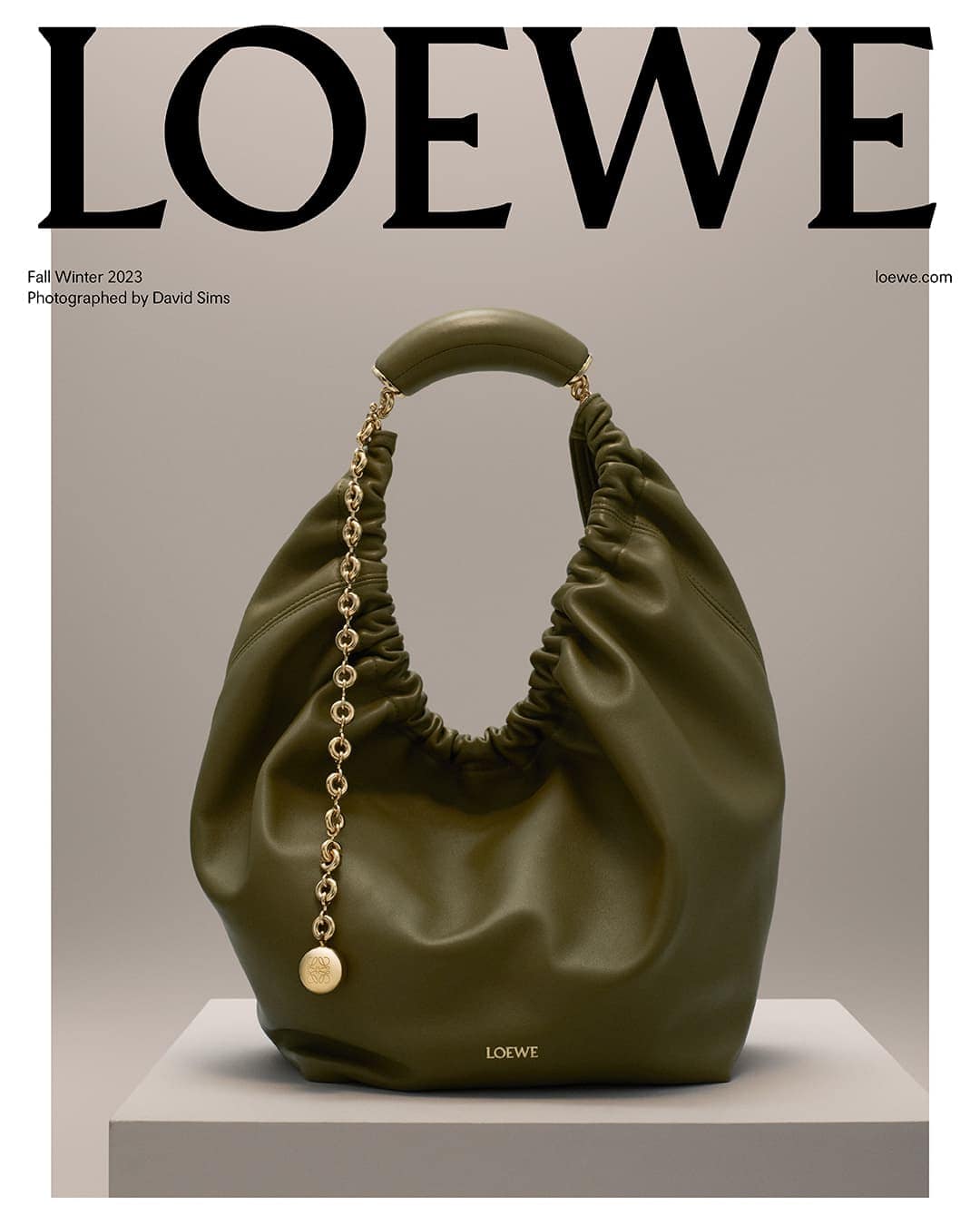 Olive green Loewe hobo bag on a grey platform, featuring a chain detail and set against a grey backdrop with the Loewe logo.