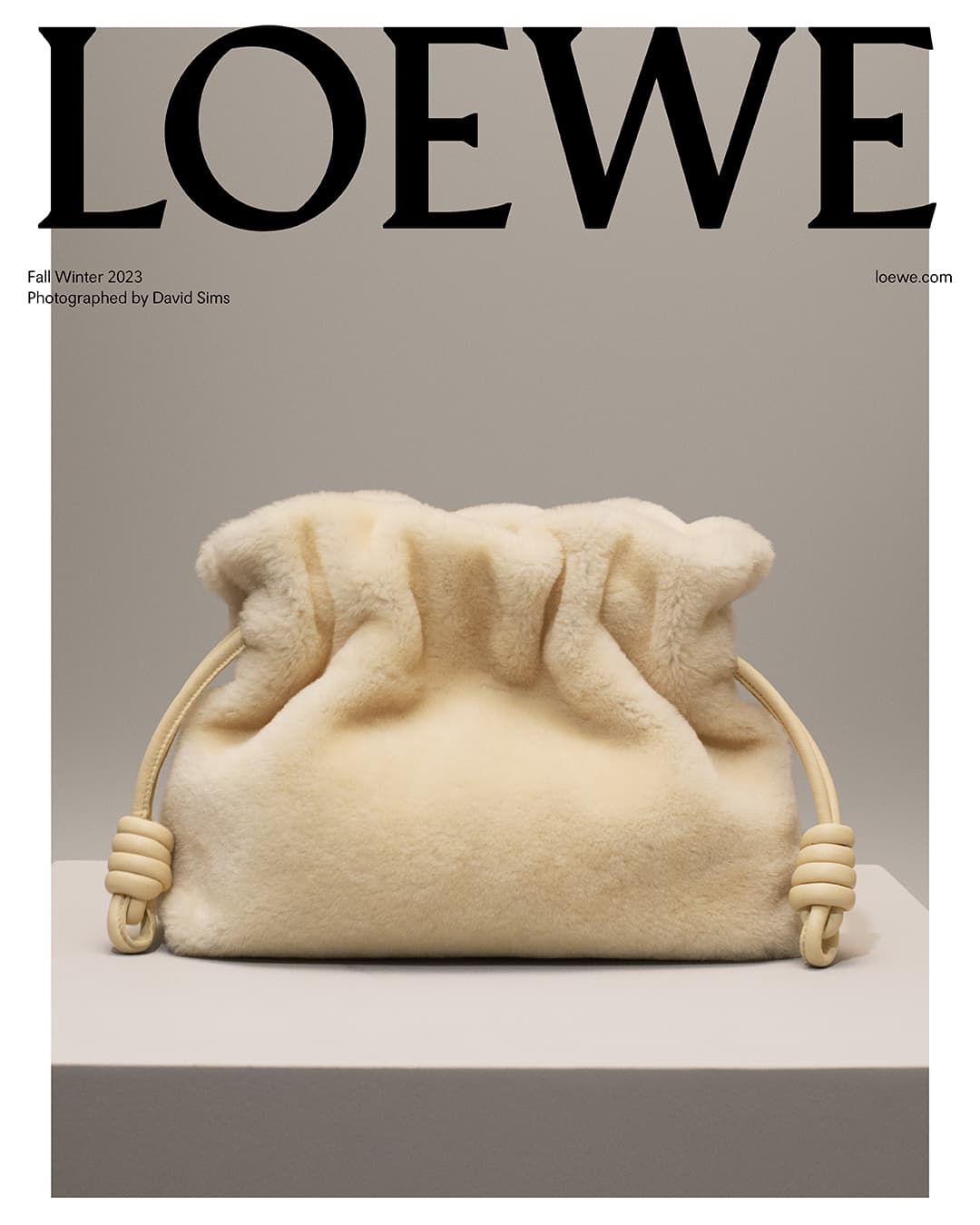 Ivory Loewe shearling pouch bag on a platform against a taupe background, presented in a studio fashion shot for Fall/Winter 2023.