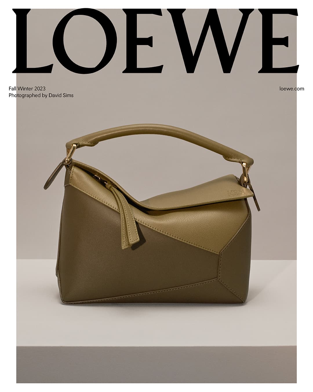 Olive green Loewe Puzzle bag in neutral studio, featuring angular leather panels, top handle, and brand logo in background.