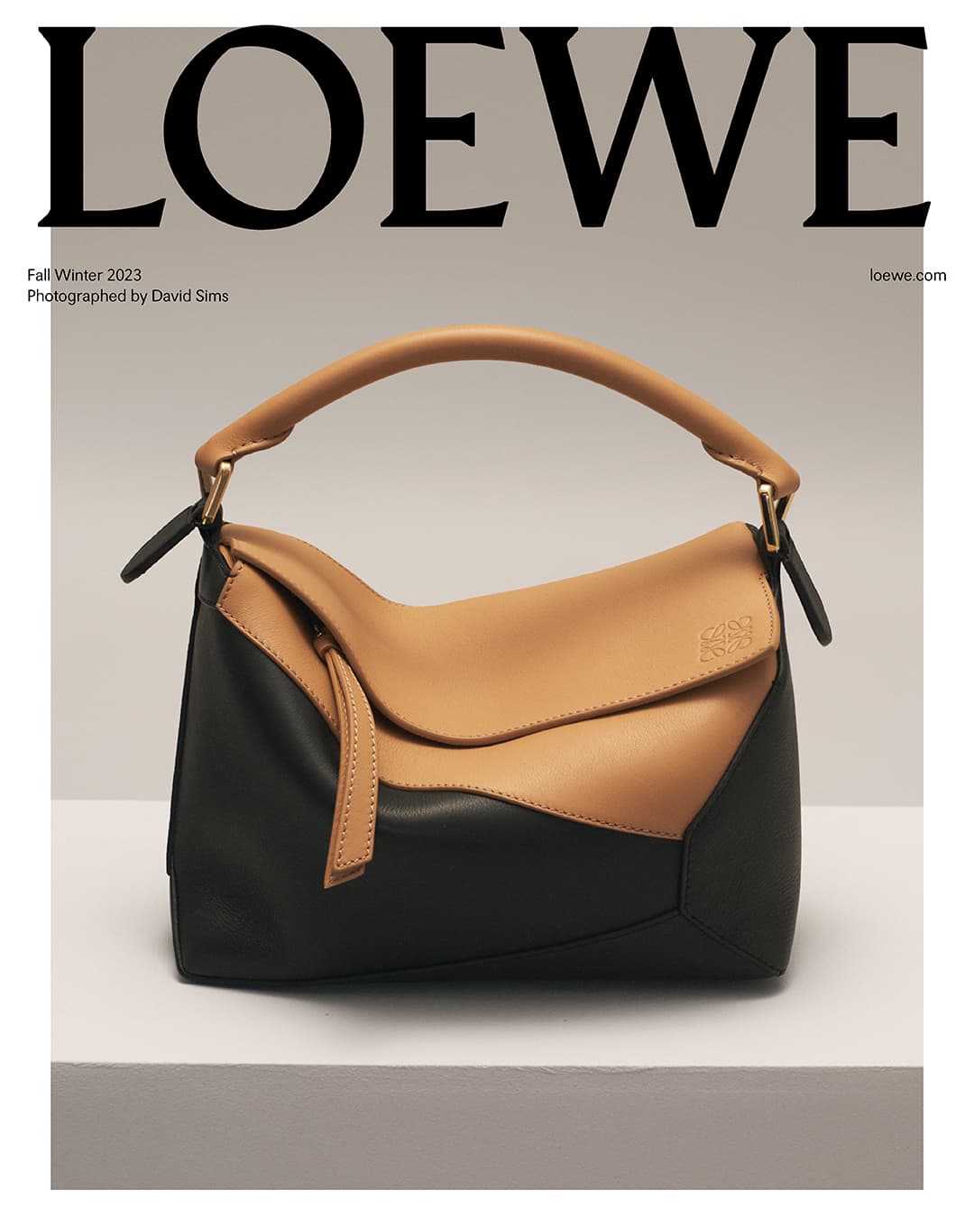 Loewe Puzzle bag in tan and black leather on a white platform, against a beige background with brand text visible above.