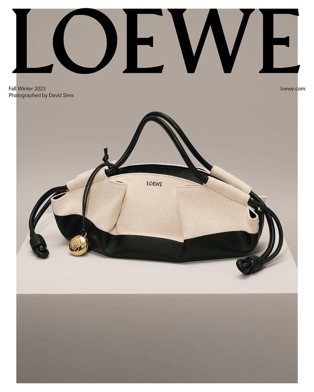Loewe cream and black leather drawstring handbag displayed on a white surface with a gray background, fashion editorial shot.