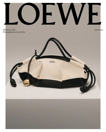 Loewe cream and black leather drawstring handbag displayed on a white surface with a gray background, fashion editorial shot.
