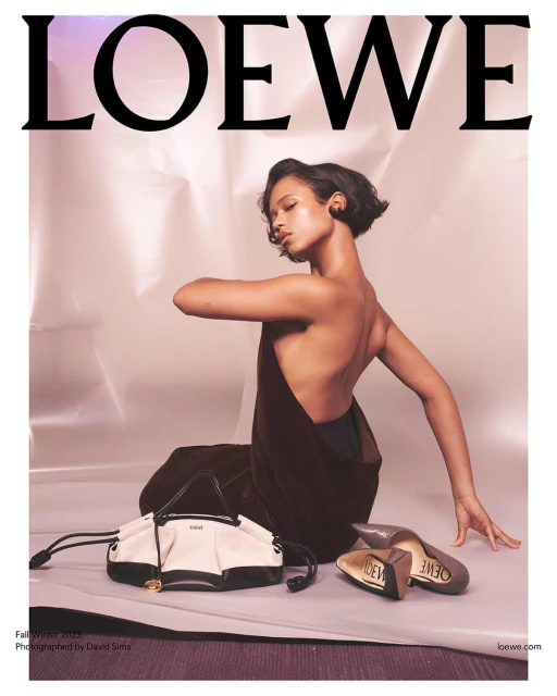 Fashion editorial featuring a model posing with Loewe accessories in a studio with a pink and silver backdrop.