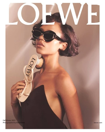 Model wearing dark sunglasses and holding a cream sandal near her chin for the Loewe Fall 2023 ad campaign by David Sims.