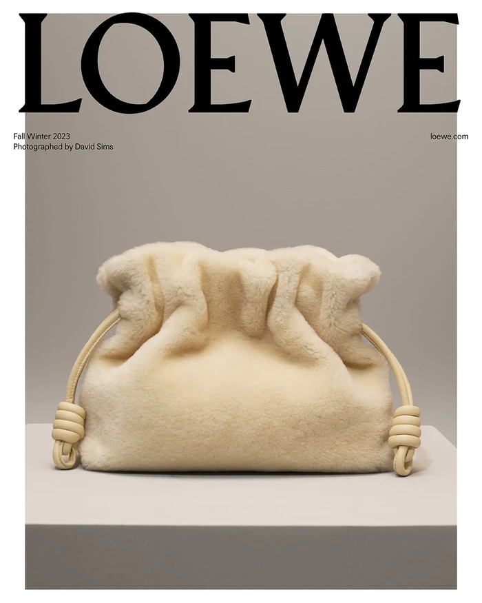 Loewe off-white shearling Flamenco clutch handbag with knotted drawstring pulls resting on a display plinth in a studio setting.