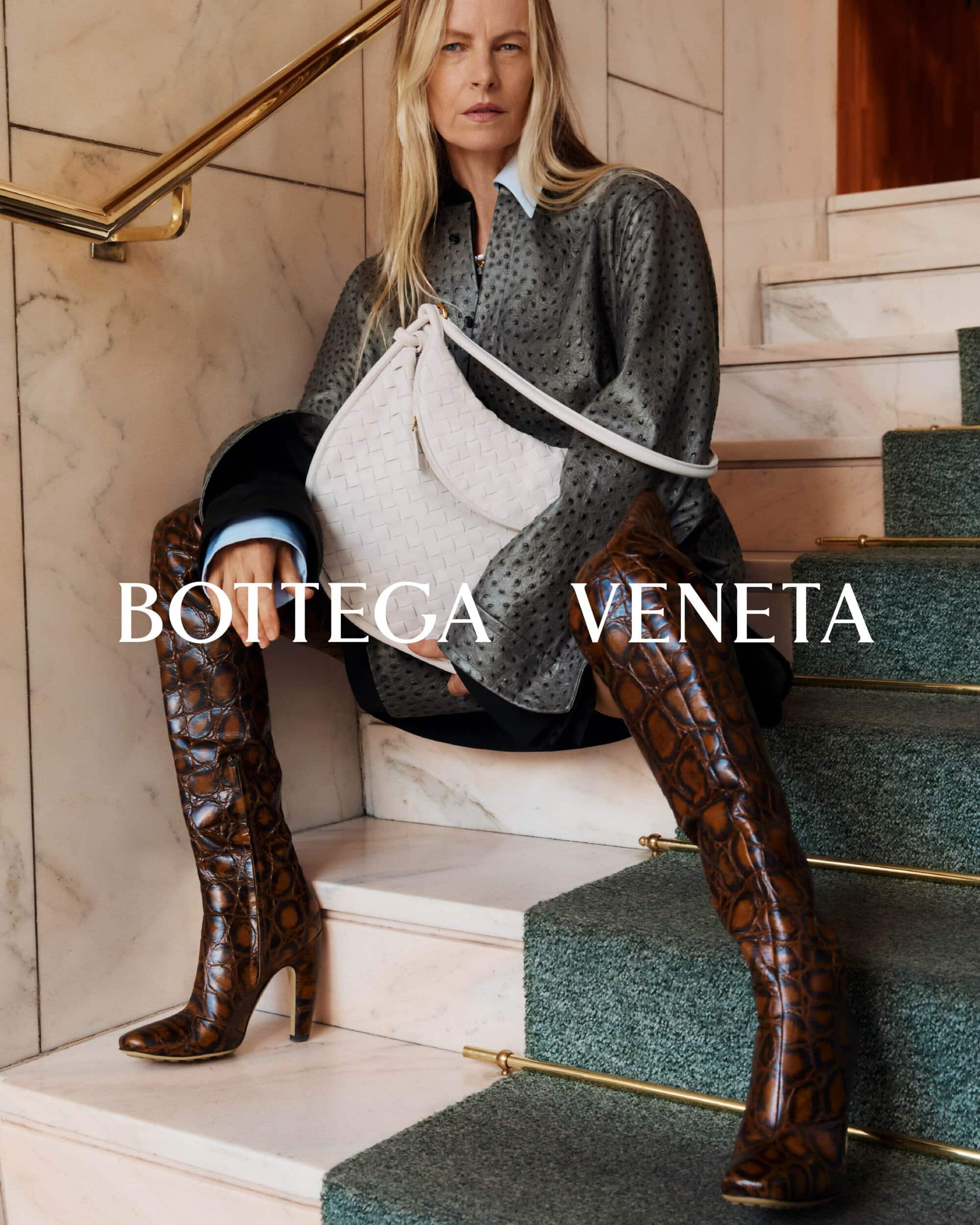 Fashion editorial shot of a woman in thigh-high snake-print boots, holding a white bag on carpeted stairs, promoting Bottega Veneta.