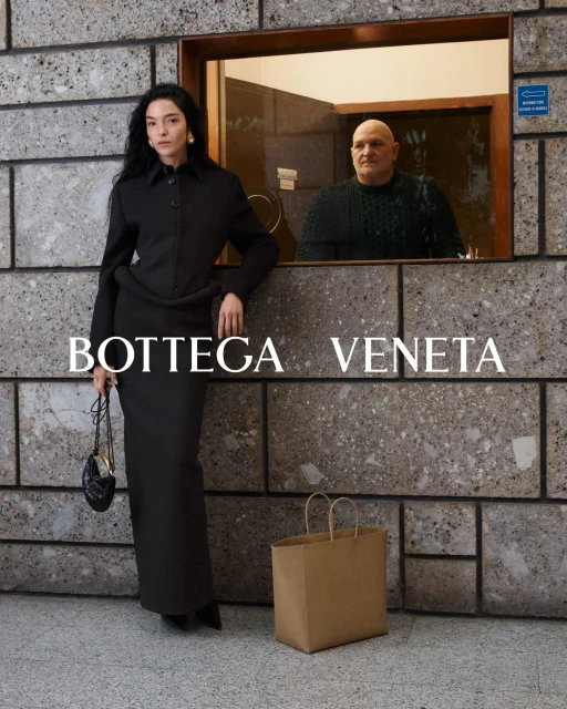Fashion shot features a woman in a long black dress next to a man in a window, with a brown shopping bag on the floor and brand text overlay.