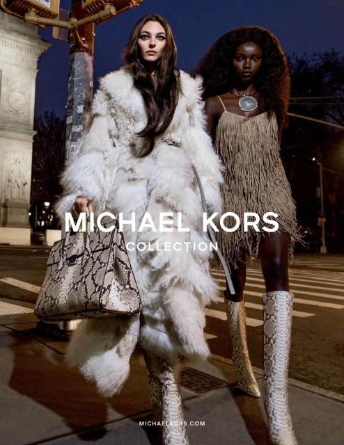 Two fashion models pose outdoors at night in Michael Kors designs: a fur coat, snake boots, snakeskin handbag, and a fringe dress.