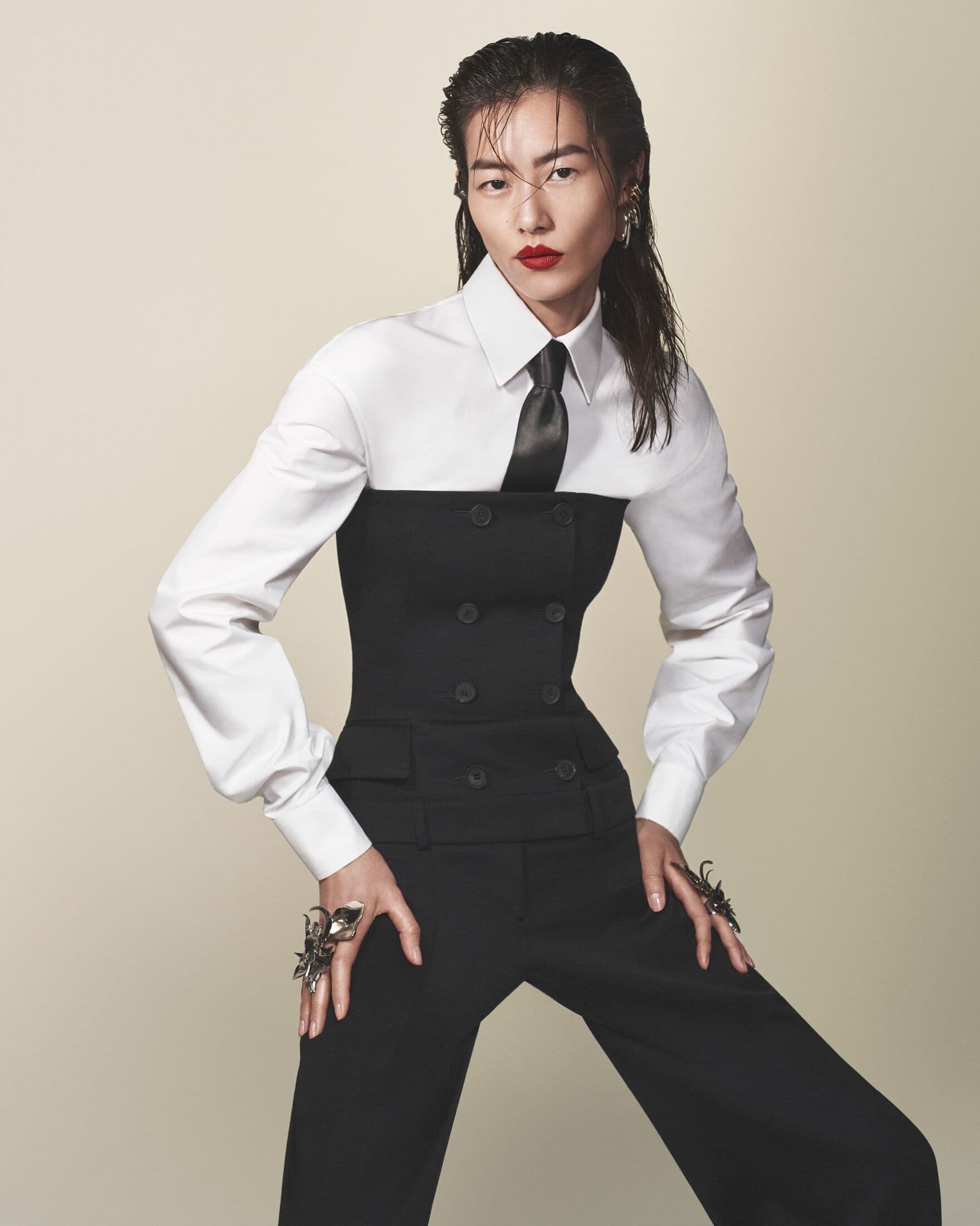 Fashion portrait of an Asian woman wearing a black and white suit with tie in a studio with spiderweb rings on her hands.