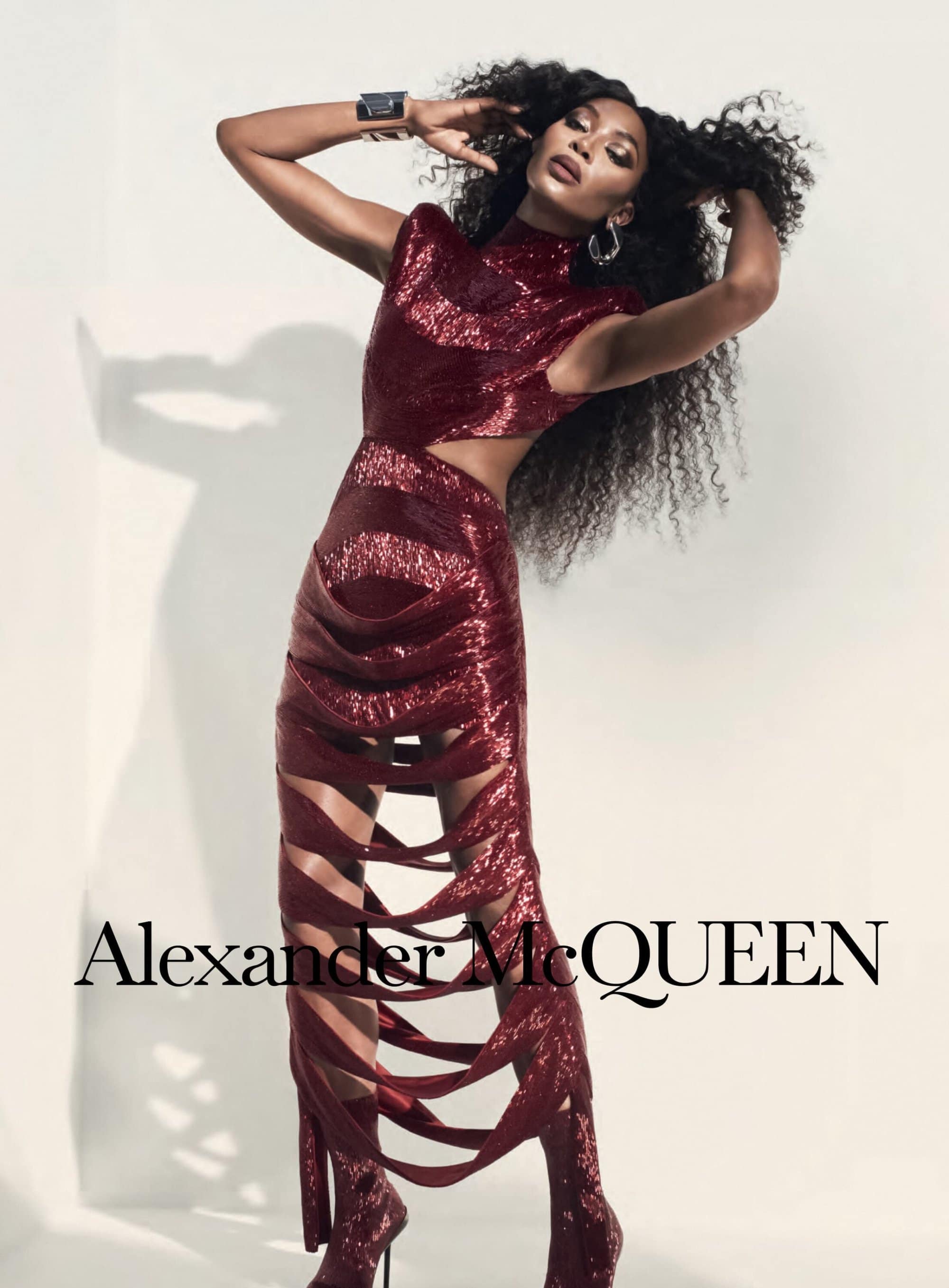 A slender Black female model poses in a studio wearing a burgundy sequined dress and matching heeled boots. Alexander McQueen logo.