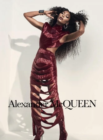 A slender Black female model poses in a studio wearing a burgundy sequined dress and matching heeled boots. Alexander McQueen logo.