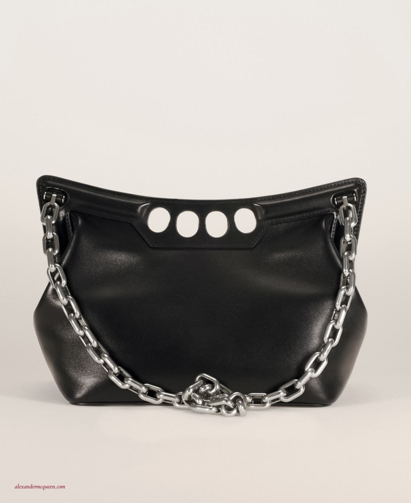 Black leather shoulder bag with a silver chain strap and four white circles, set against a light neutral studio background.