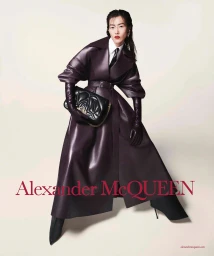 Liu Wen in a dark burgundy leather trench coat and opera gloves holding a black clutch for Alexander McQueen Fall 2023.