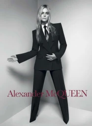 Elle Fanning in a black tailored suit and tie against a pale studio background for Alexander McQueen