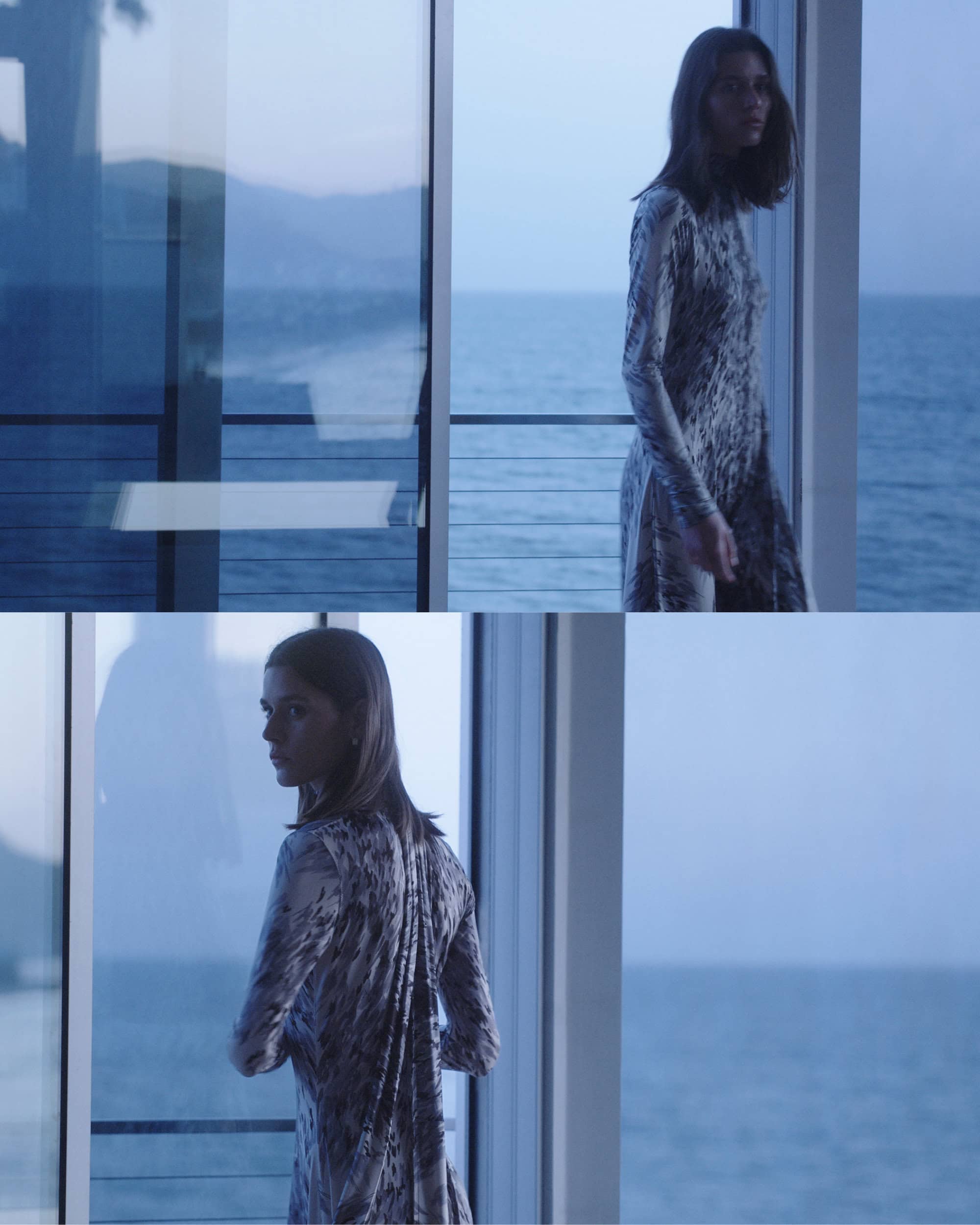 Two women in patterned dresses stand near glass doors overlooking the ocean, in a muted, atmospheric fashion or lifestyle scene.