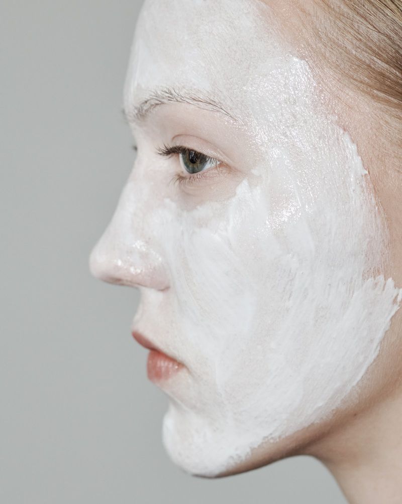 Close-up profile of a woman's face covered in a white skincare mask, showcasing beauty and personal care in a studio setting.