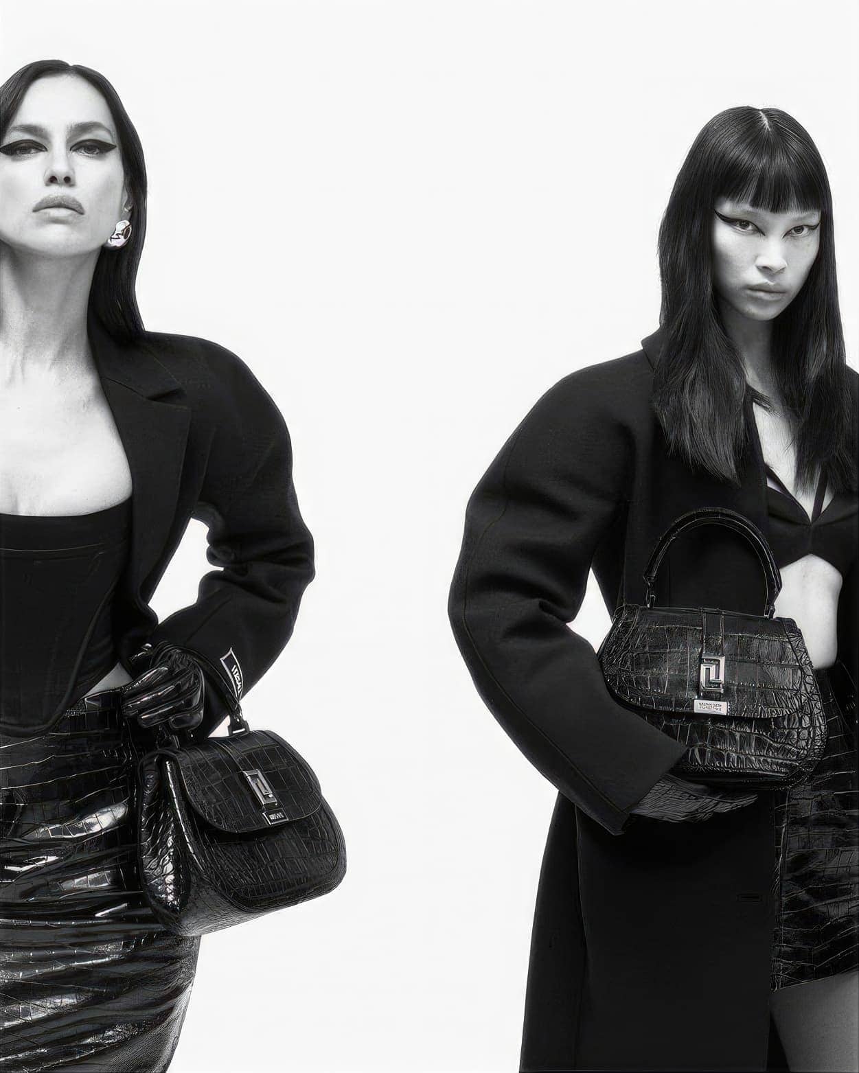Black and white studio shot of two women in fashionable black clothing holding matching black crocodile-skin handbags.