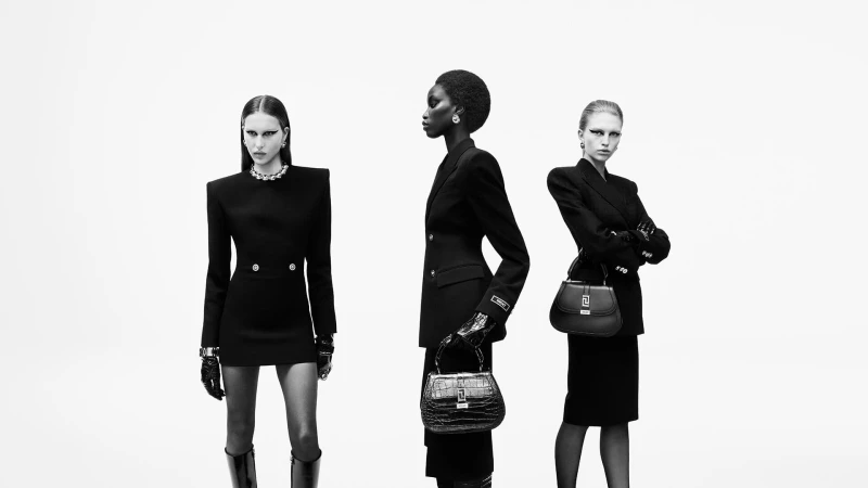 Three women in black tailored outfits and accessories pose against a white background in a studio shot, showcasing fashion and style.