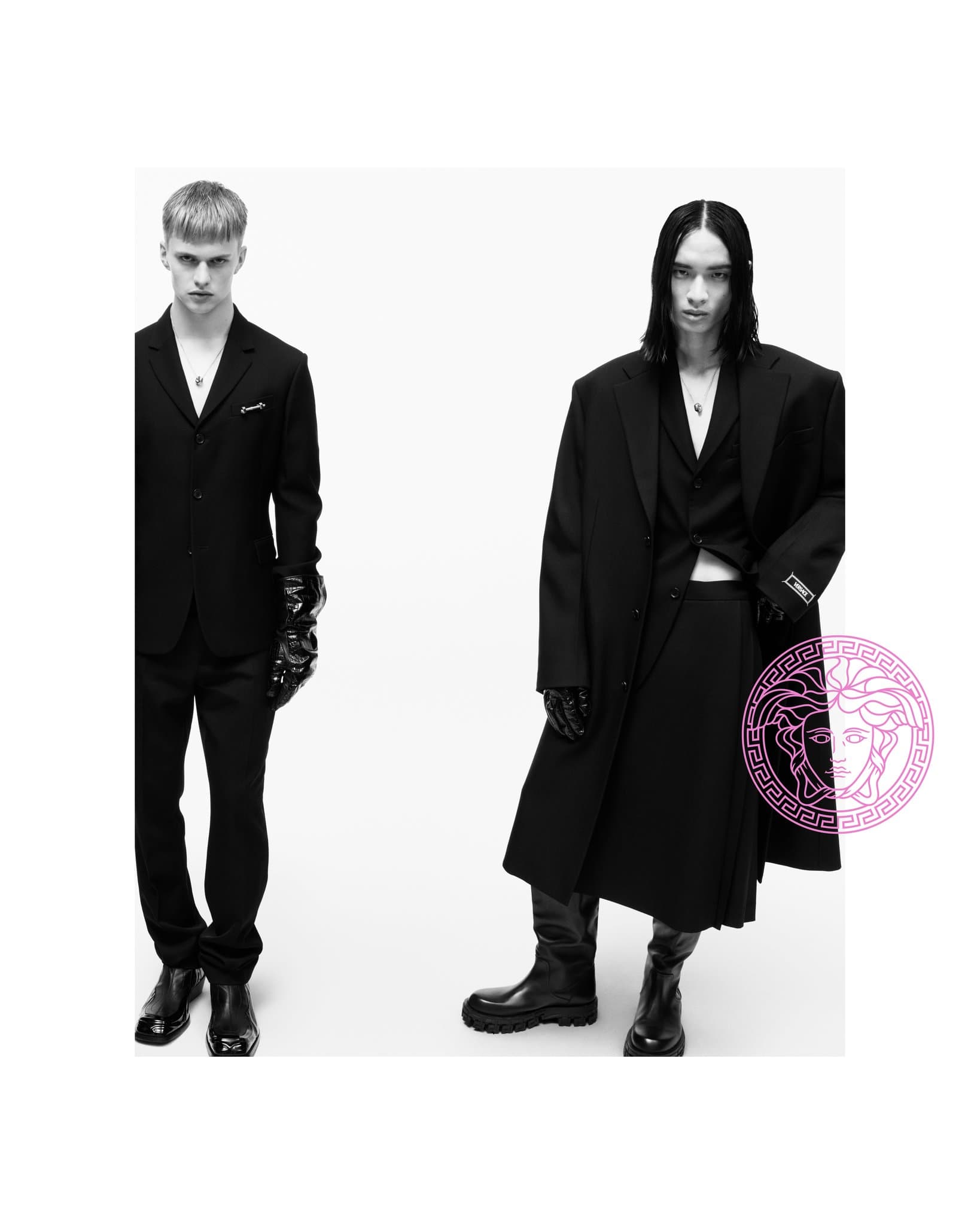 Two adult men pose in black suits and boots against a white backdrop for a fashion editorial, showcasing elegant and modern menswear.