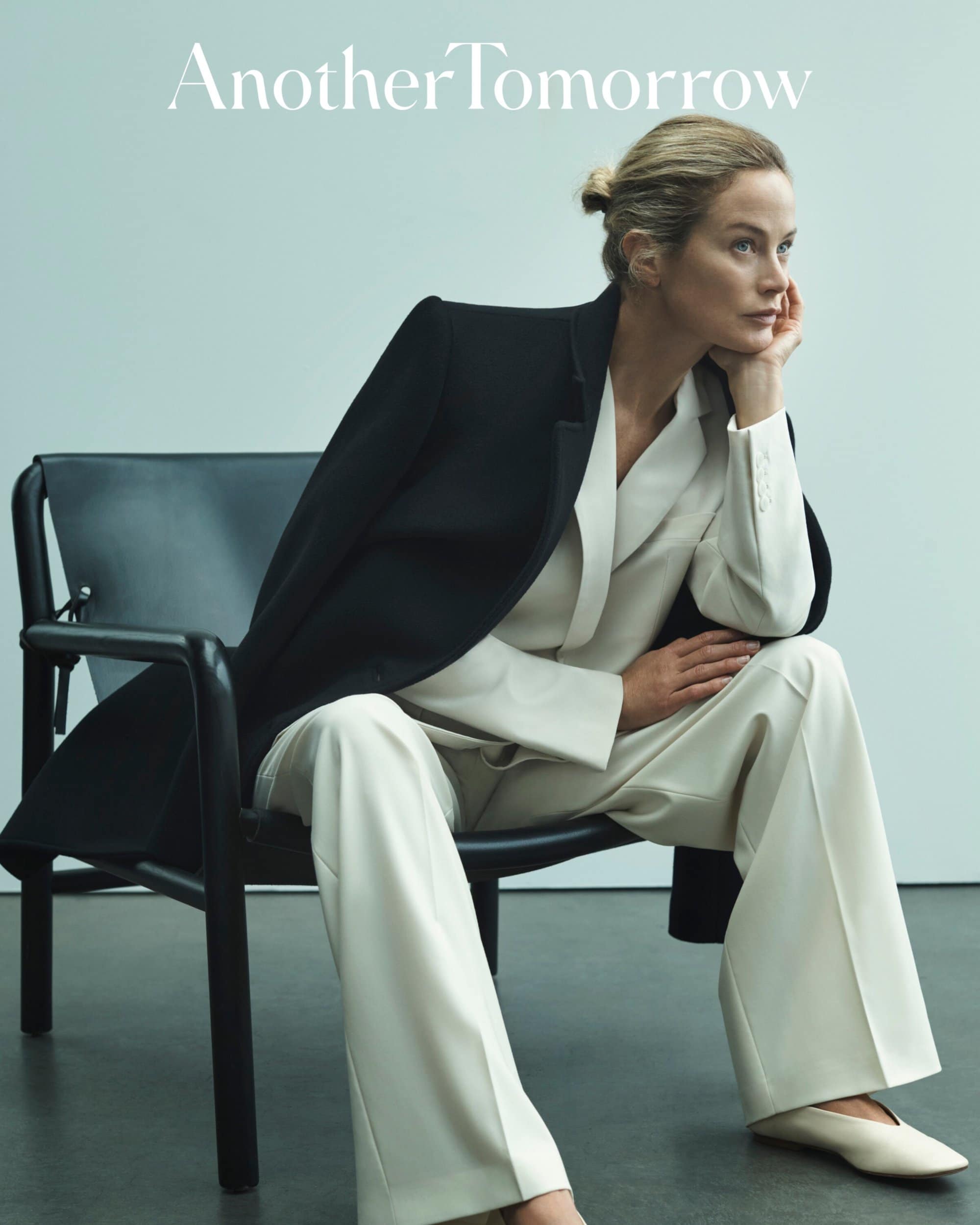 Adult female seated on a chair, looking right, wearing a beige suit with black blazer in a photo studio setting. Text overlay.