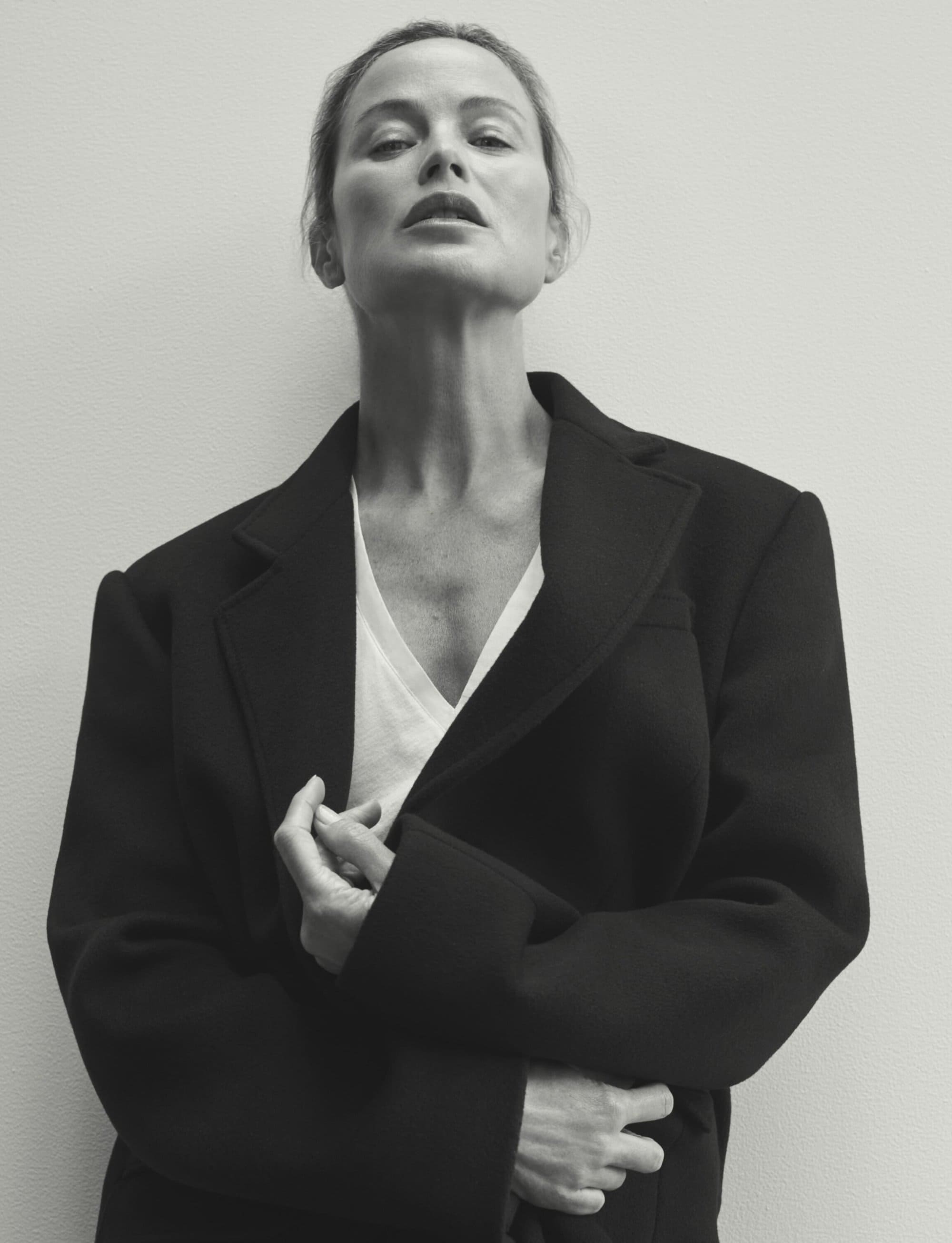 Monochrome portrait of an adult woman wearing a dark blazer and white v-neck shirt against a light background, posing in a studio.